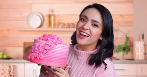 Mujer sonriendo con pastel rosa en cocina.