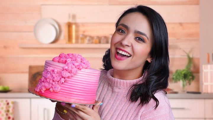 Mujer sonriendo con pastel rosa en cocina.